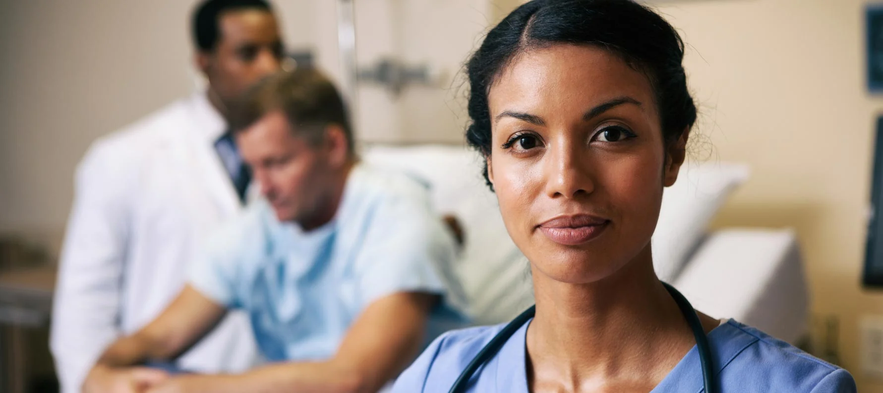 A nurse standing in a clinical setting with colleagues in the background